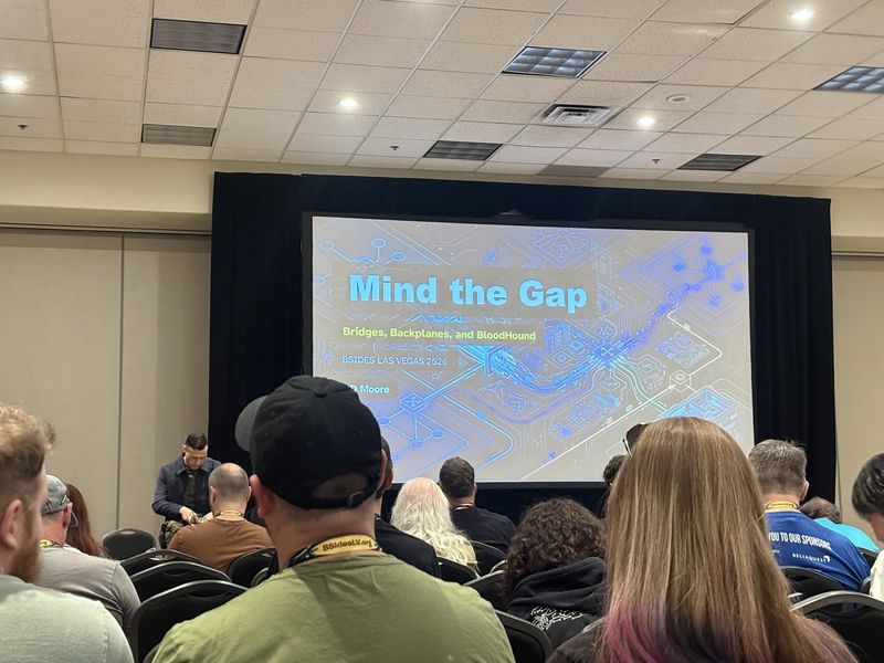 Slide: Title slide for Mind the Gap, Bridges, Backplanes, and BloodHound by HD Moore at BSides Las Vegas 2026, over an illustration of interconnected network and industrial protocol paths